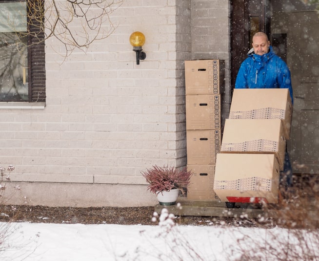 A man in a blue jacket rolls several large boxes on a dolly