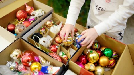 Young child stands in front of open boxes of bright, colorful ornaments.
