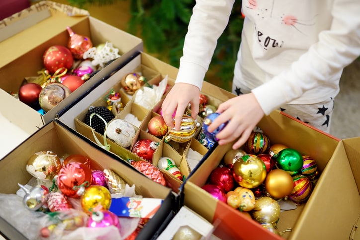 Young child stands in front of open boxes of bright, colorful ornaments.