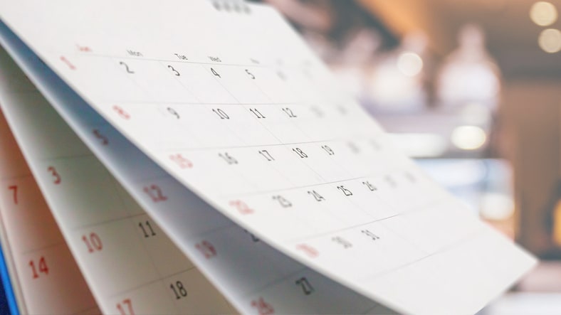 A close-up calendar has the first pages lifted to reveal future months.