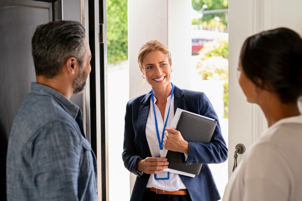 A couple welcomes a real estate agent into their home through the front door