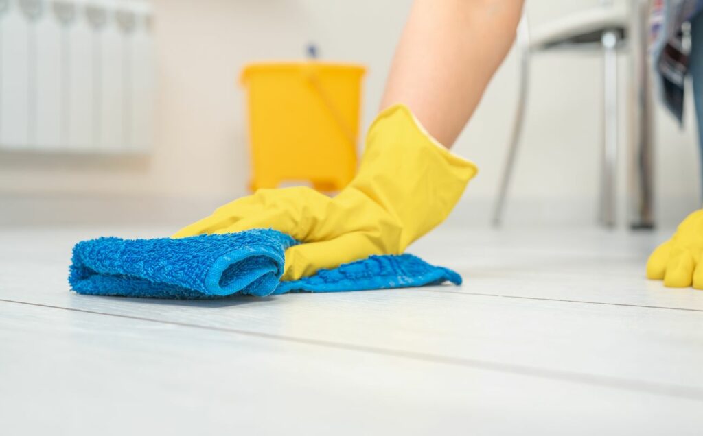 A hand in a glove using a wet rag to clean the tile floor