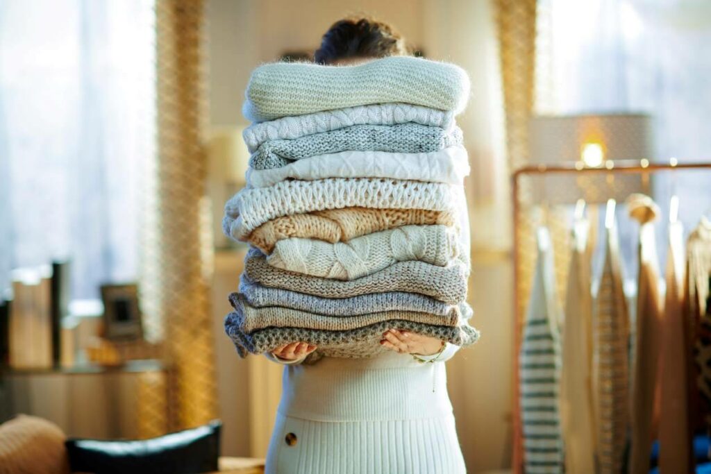 A woman holding a lot of knit sweaters. 