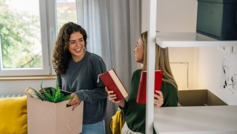 Two women carrying moving boxes out of their room