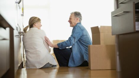 A older couple sitting on the floor next to their packed boxes