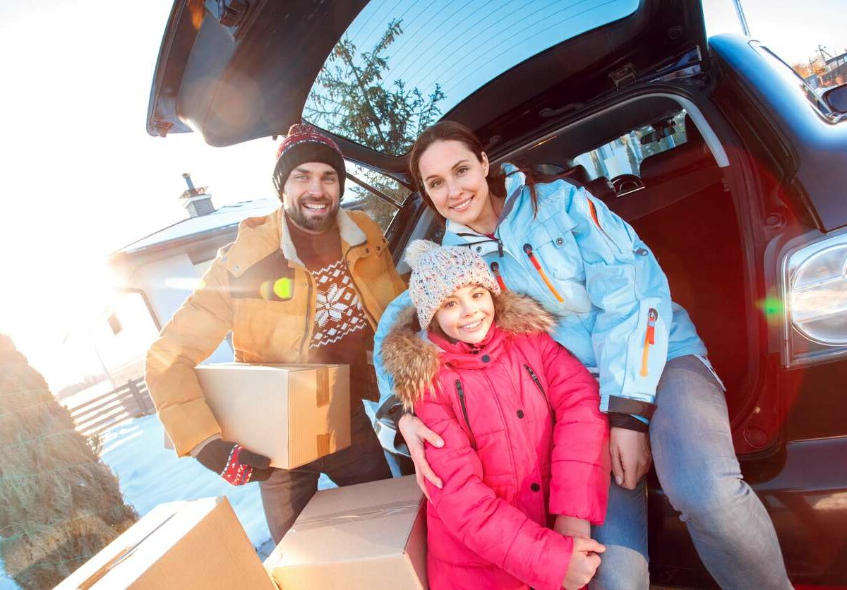 Family dressed in winter clothing behind a car with storage boxes ready to move.