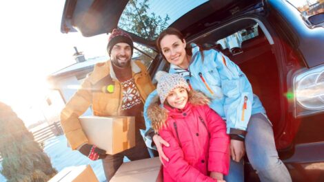 Family dressed in winter clothing behind a car with storage boxes ready to move.