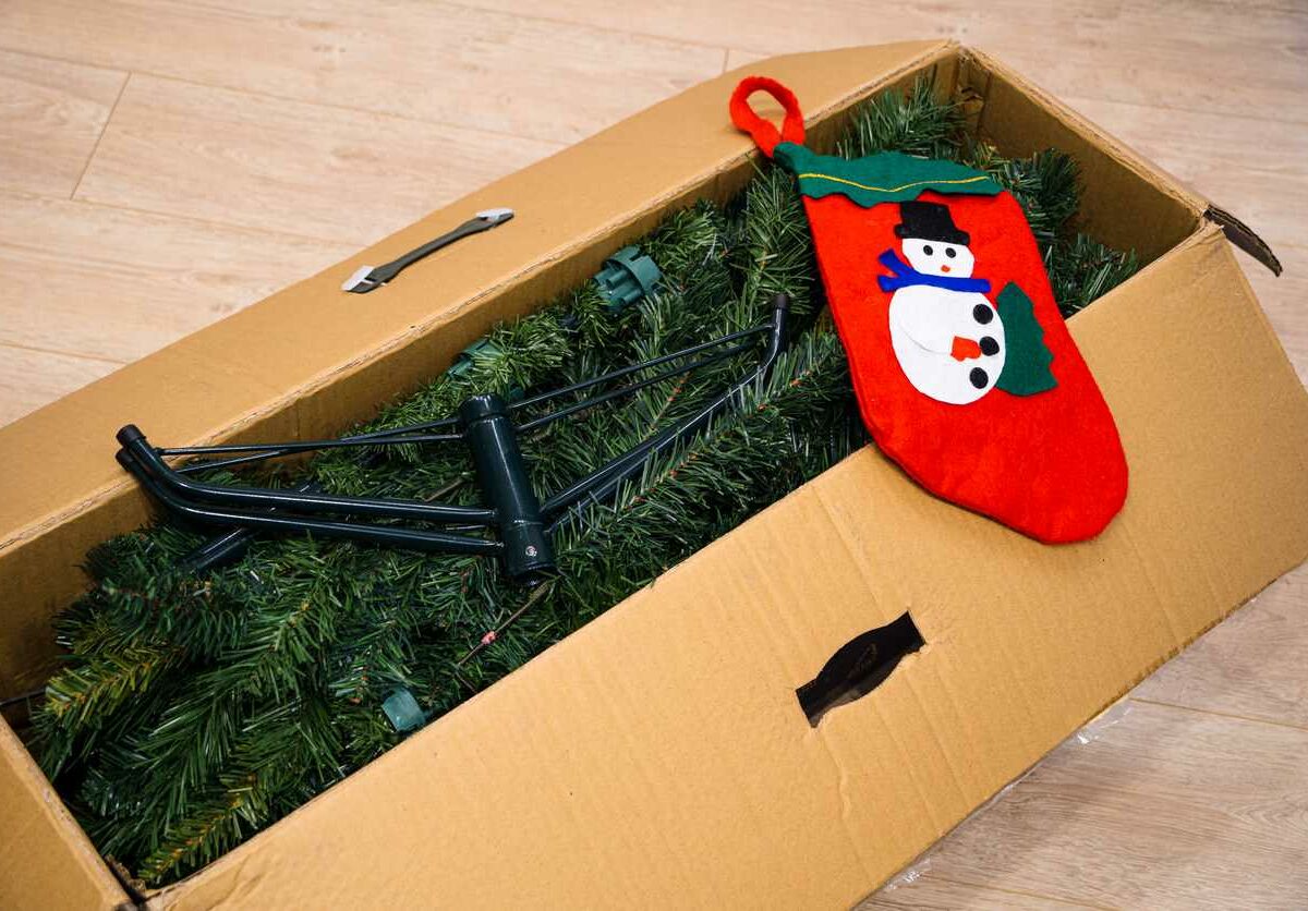An artificial Christmas tree packed into a box along with a stocking with a snowman on it.
