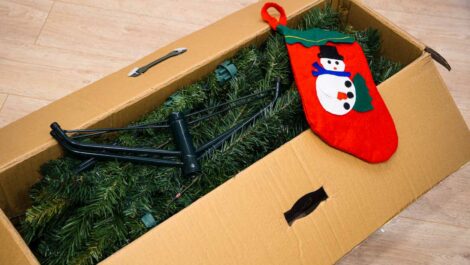 An artificial Christmas tree packed into a box along with a stocking with a snowman on it.