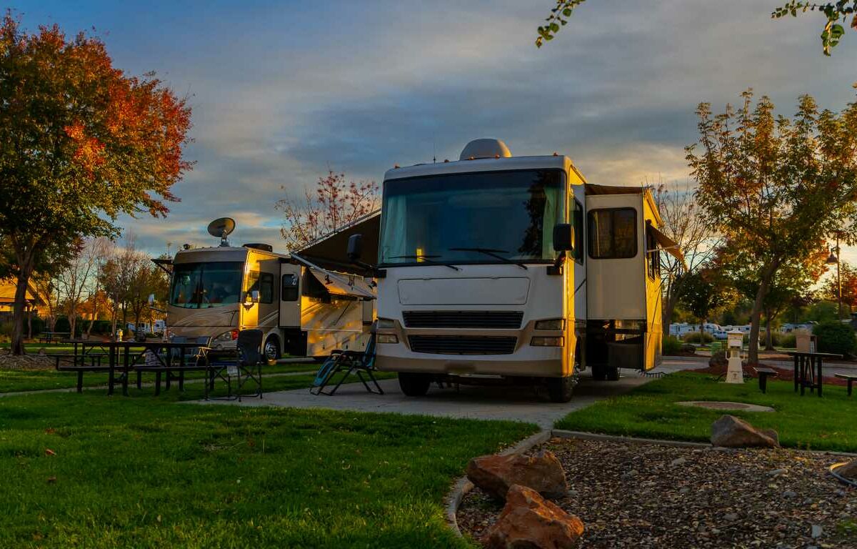 Two RVs parked at a campsite during autumn at sunset.