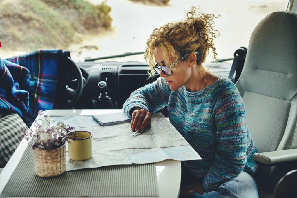 A woman sitting at a table in an RV marking on a map with a pen as she plans her trip.