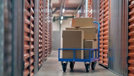 A cart of boxes in the hallway of a storage facility surrounded by orange storage unit doors