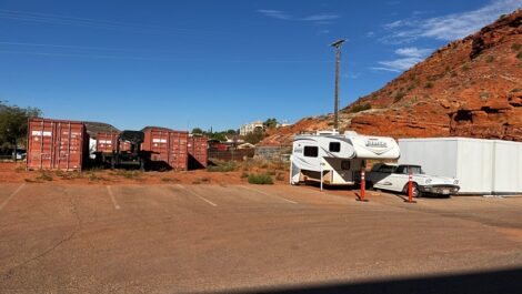 Outdoor parking spots with a small camper and nice white car near red rocks.