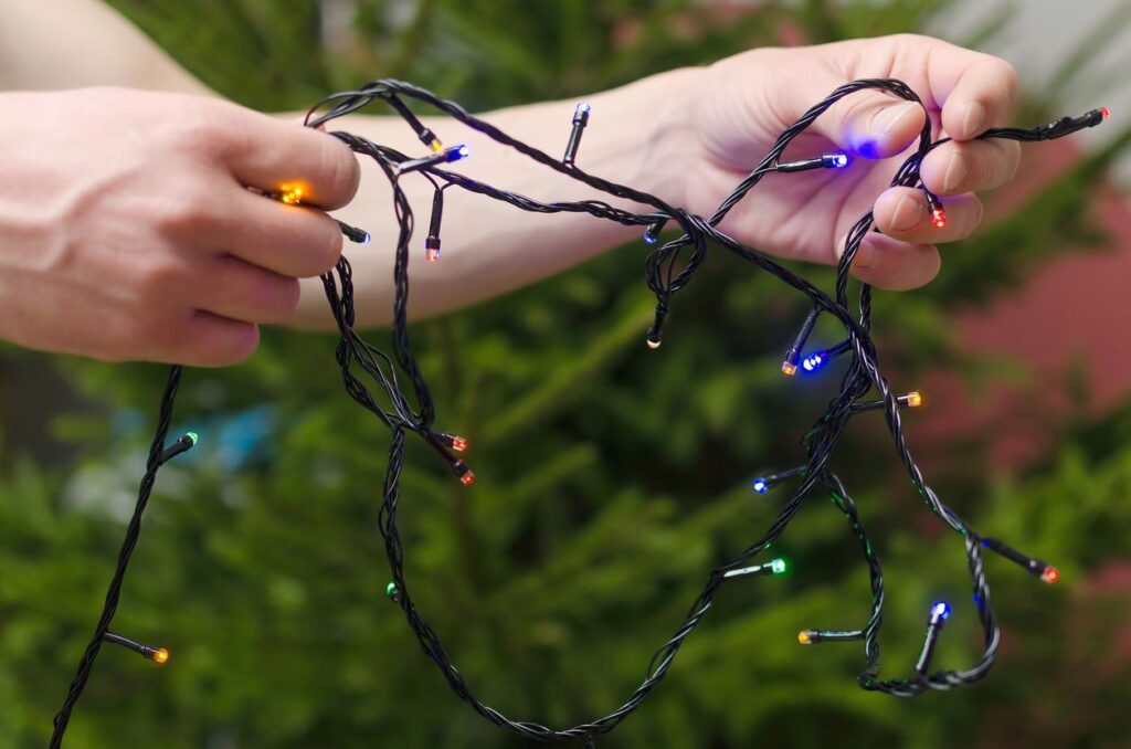 Two hands holding a string of colorful Christmas lights outdoors.