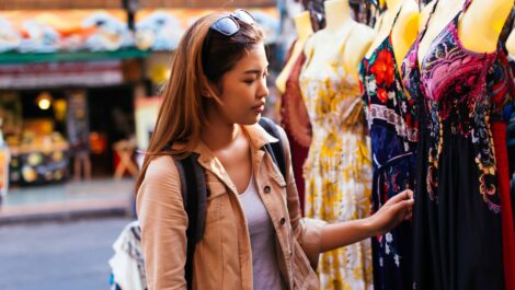 A young woman browses vintage dresses at a flea market.