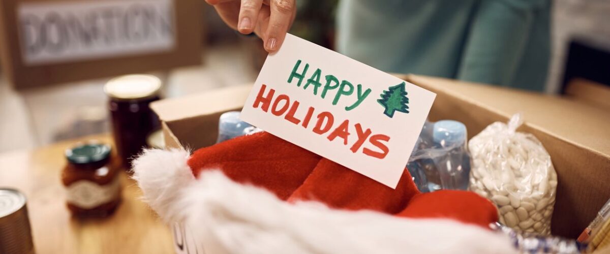 A male volunteer places a "Happy Holidays" card in a donation box filled with holiday items and canned food.