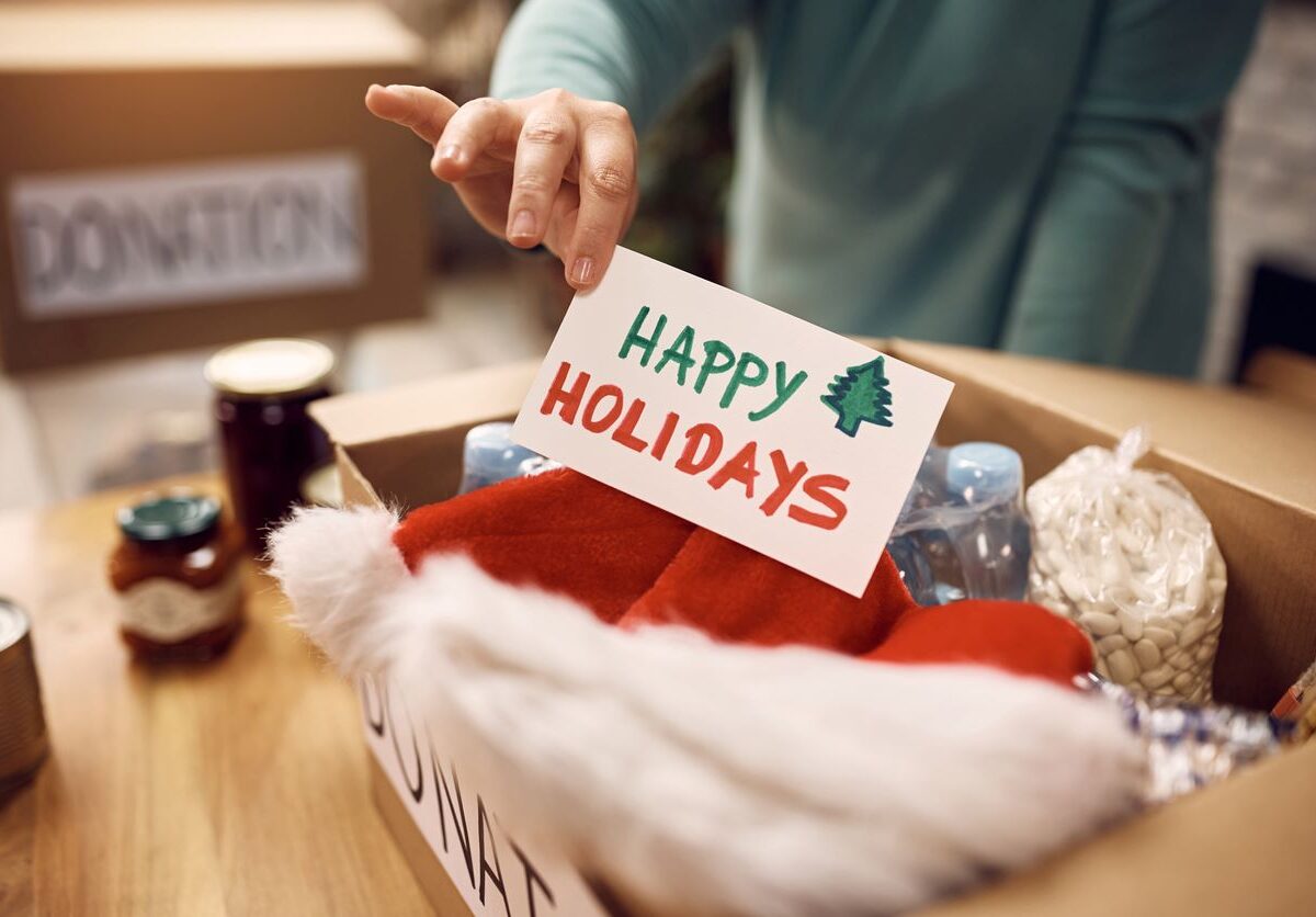 A male volunteer places a "Happy Holidays" card in a donation box filled with holiday items and canned food.