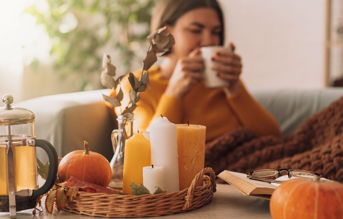 A young woman drinks tea in her living room, decorated with fall touches.