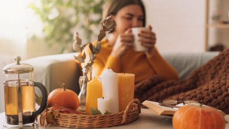 A young woman drinks tea in her living room, decorated with fall touches.