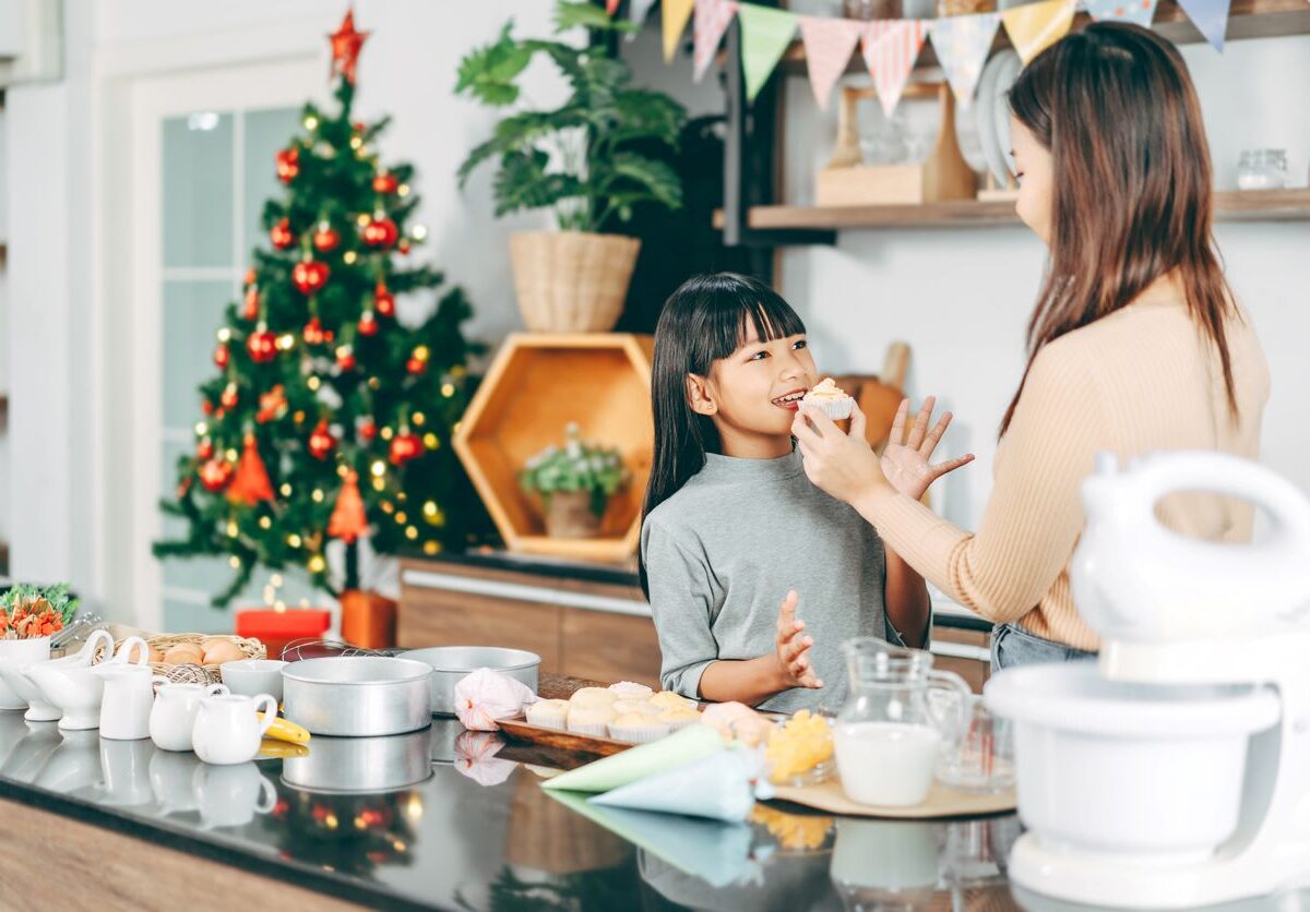 A mother and daughter enjoy baking together in a festive kitchen decorated for Christmas.