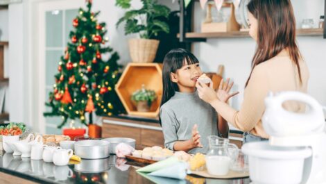 A mother and daughter enjoy baking together in a festive kitchen decorated for Christmas.