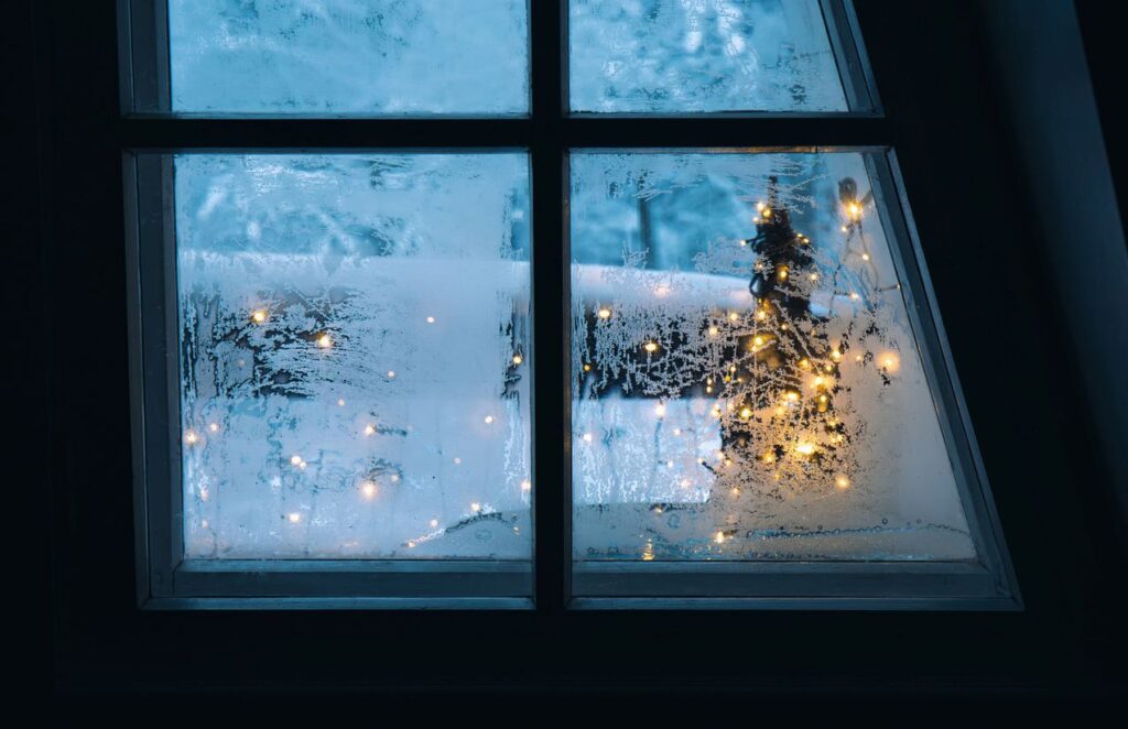 A frosted window with twinkling Christmas lights outside.