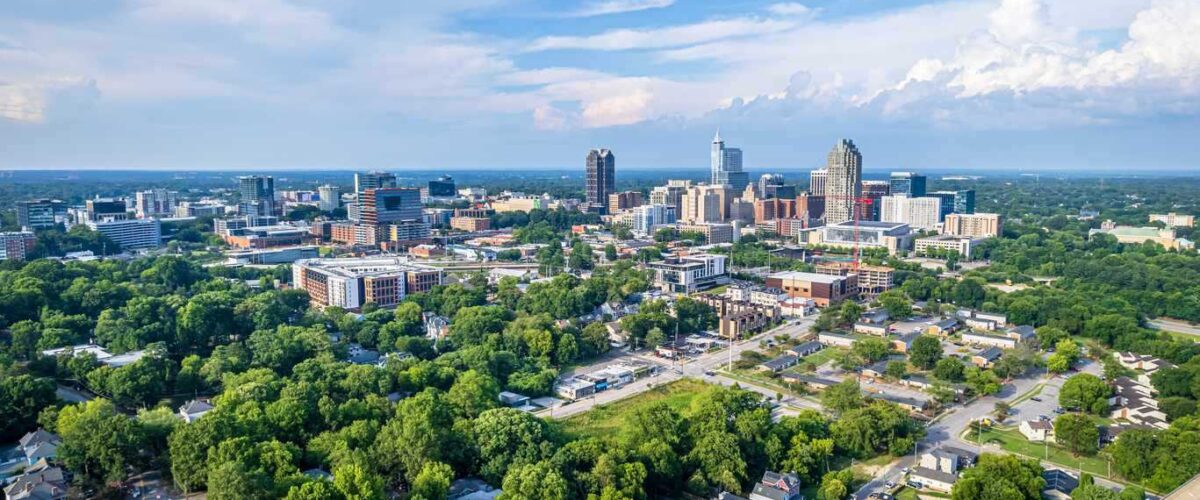 Downtown Raleigh, NC, showcasing skyscrapers and lush green trees.