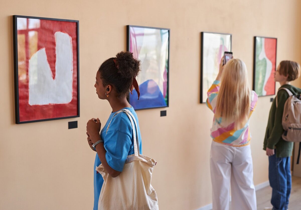 Visitors admire abstract paintings in a brightly lit art gallery.