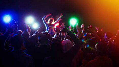 A concert crowd with hands raised for a performer in front of stage lights.