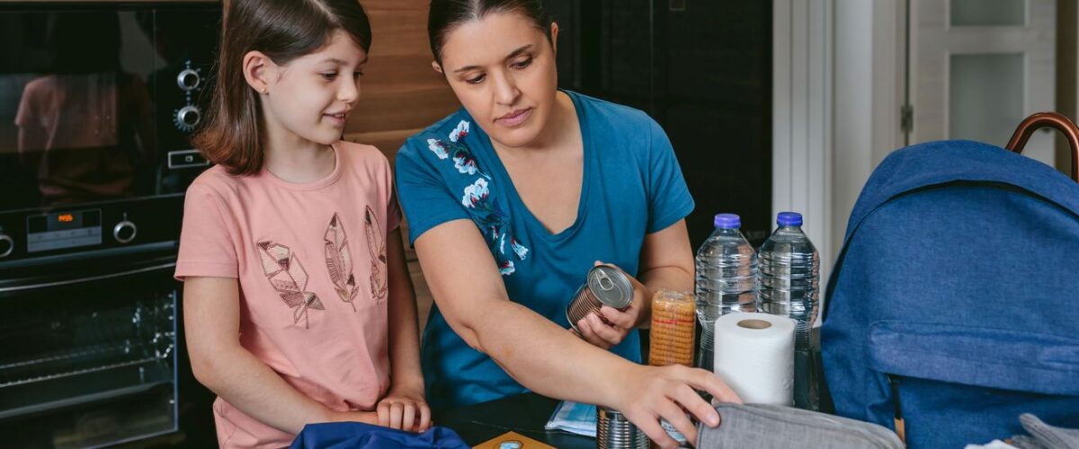 A mother and daughter packing tornado emergency supplies, including food, water, and a first aid kit.
