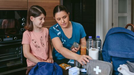 A mother and daughter packing tornado emergency supplies, including food, water, and a first aid kit.