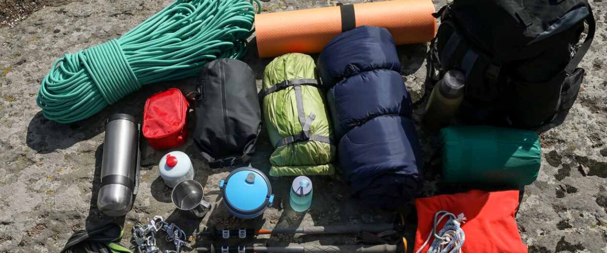 Camping gear neatly laid out on a rock surface, including ropes, sleeping bags, cooking items, and a backpack.