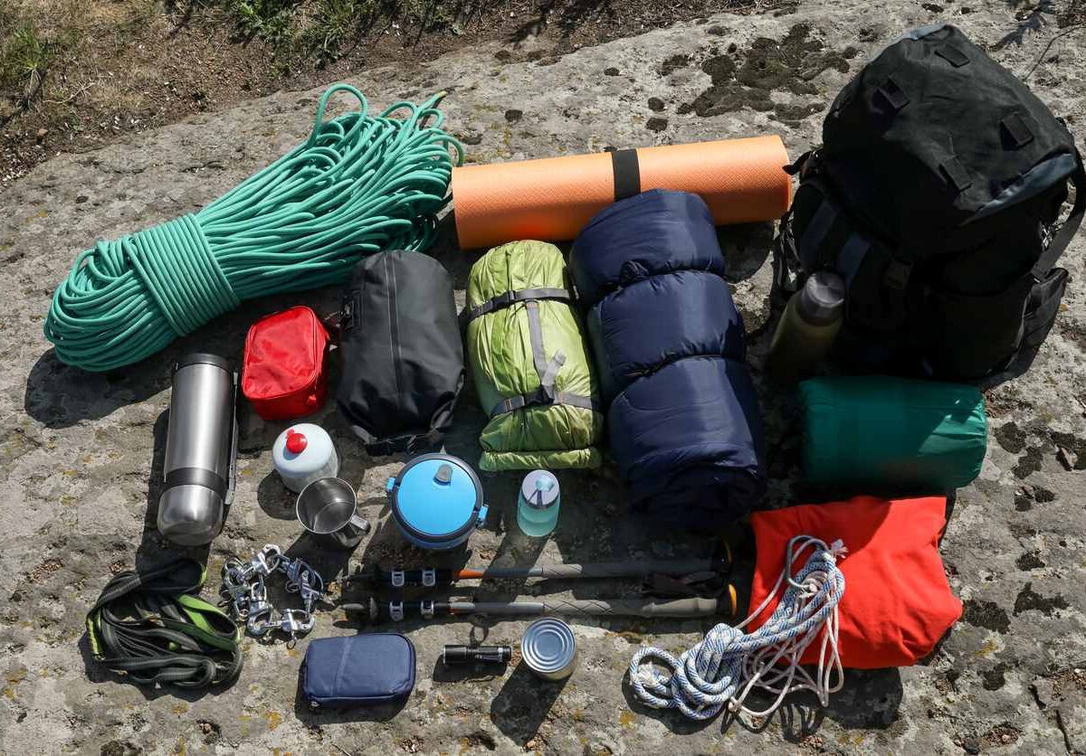 Camping gear neatly laid out on a rock surface, including ropes, sleeping bags, cooking items, and a backpack.