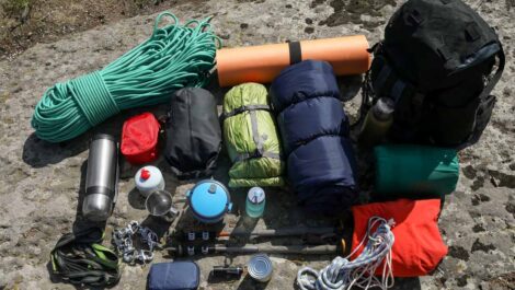 Camping gear neatly laid out on a rock surface, including ropes, sleeping bags, cooking items, and a backpack.