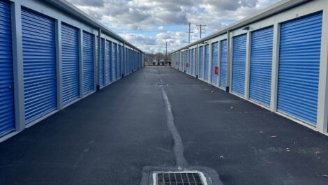 Outdoor storage units at State College Storage facility lined up on a gravel lot with beige metal buildings and multiple roll-up doors, under an overcast sky.