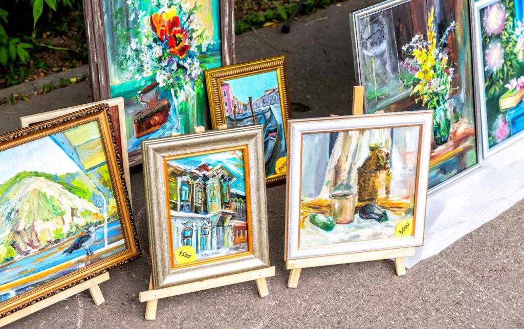 A bunch of paintings on the sidewalk.