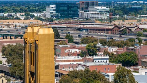 Sacramento, CA, featuring the gold Tower Bridge, downtown buildings, highways, and surrounding trees on a clear day.